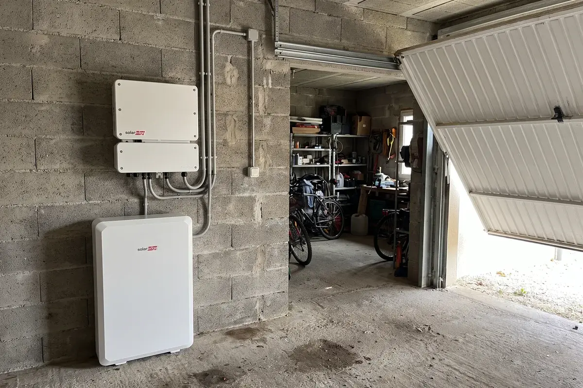 Onduleur SolarEdge Home Hub fixé au mur d’un garage en parpaing, au-dessus d’une batterie SolarEdge Home Battery posée au sol.