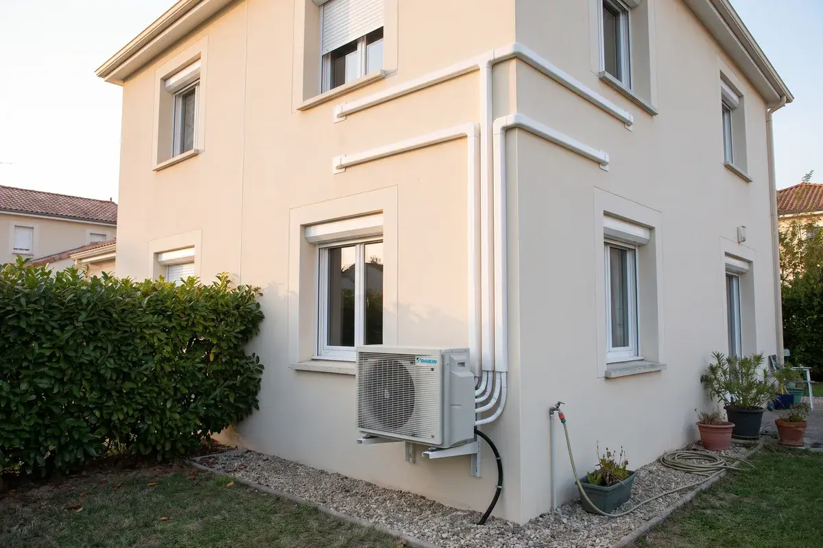 Unité extérieure multi-split Daikin MXM-A sur console, contre la façade crépie d’un pavillon, ses liaisons frigorifiques montant en goulottes vers plusieurs pièces.