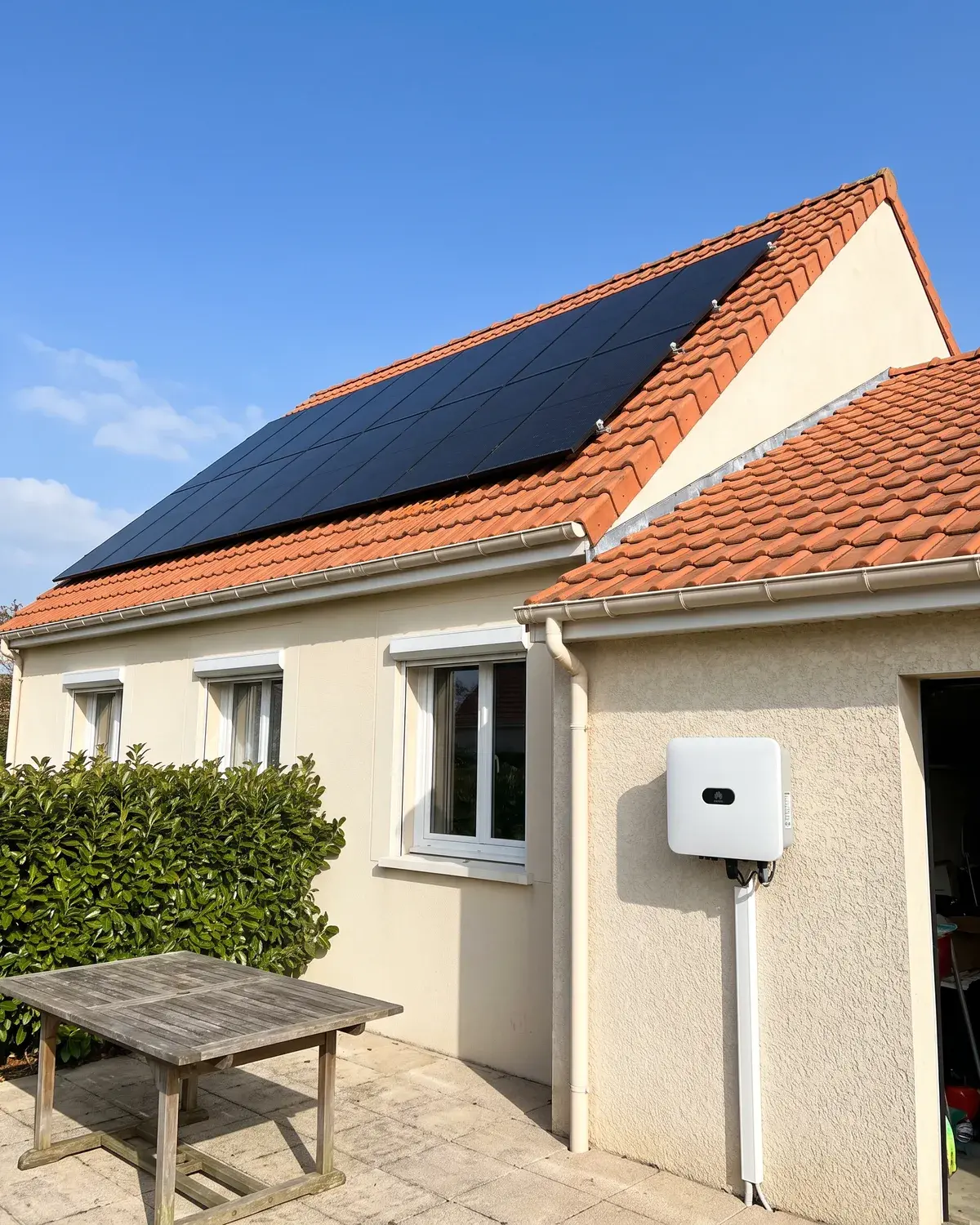 Pavillon au crépi clair avec des panneaux DualSun noirs sur le toit et un onduleur Huawei sur le mur du garage