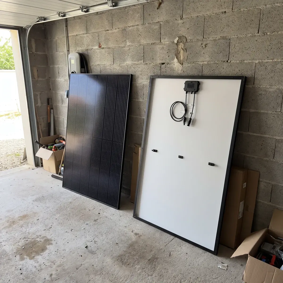 Un module AIKO NEOSTAR noir et l'arrière d'un module Trina Solar Vertex S+, appuyés contre un mur de garage.