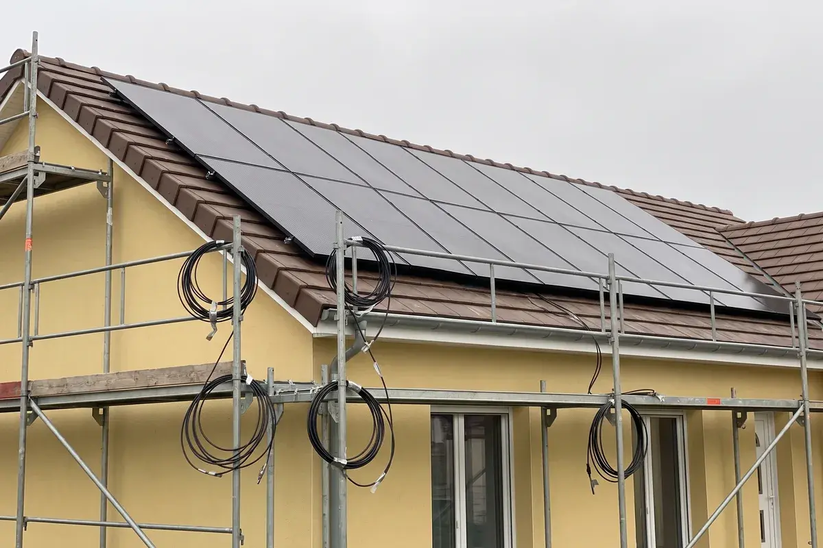 Modules Voltec Solar TARKA posés sur un pavillon en crépi jaune, échafaudage encore en place et câbles solaires enroulés, non raccordés.
