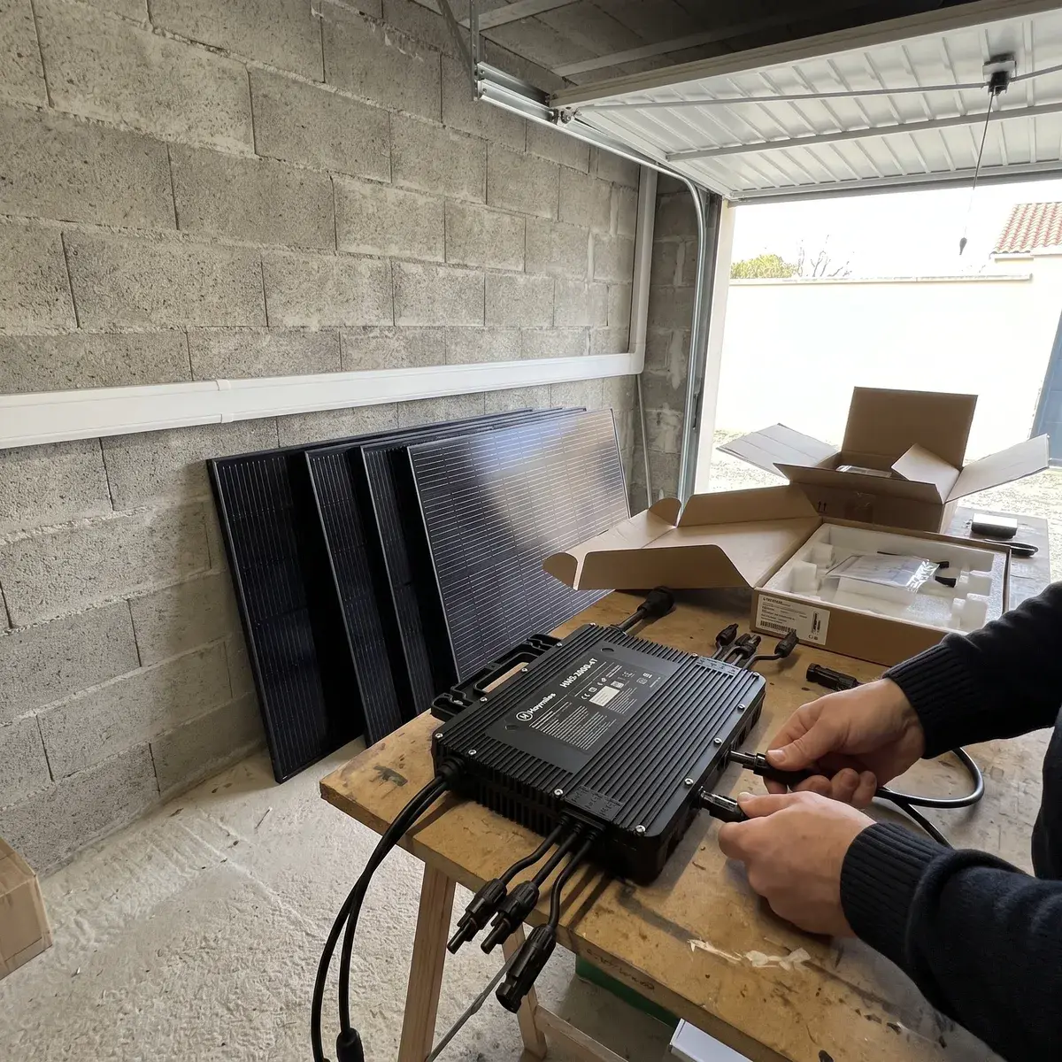 Kit d'autoconsommation déballé dans un garage : micro-onduleur Hoymiles HMS-2000-4T et modules noirs.