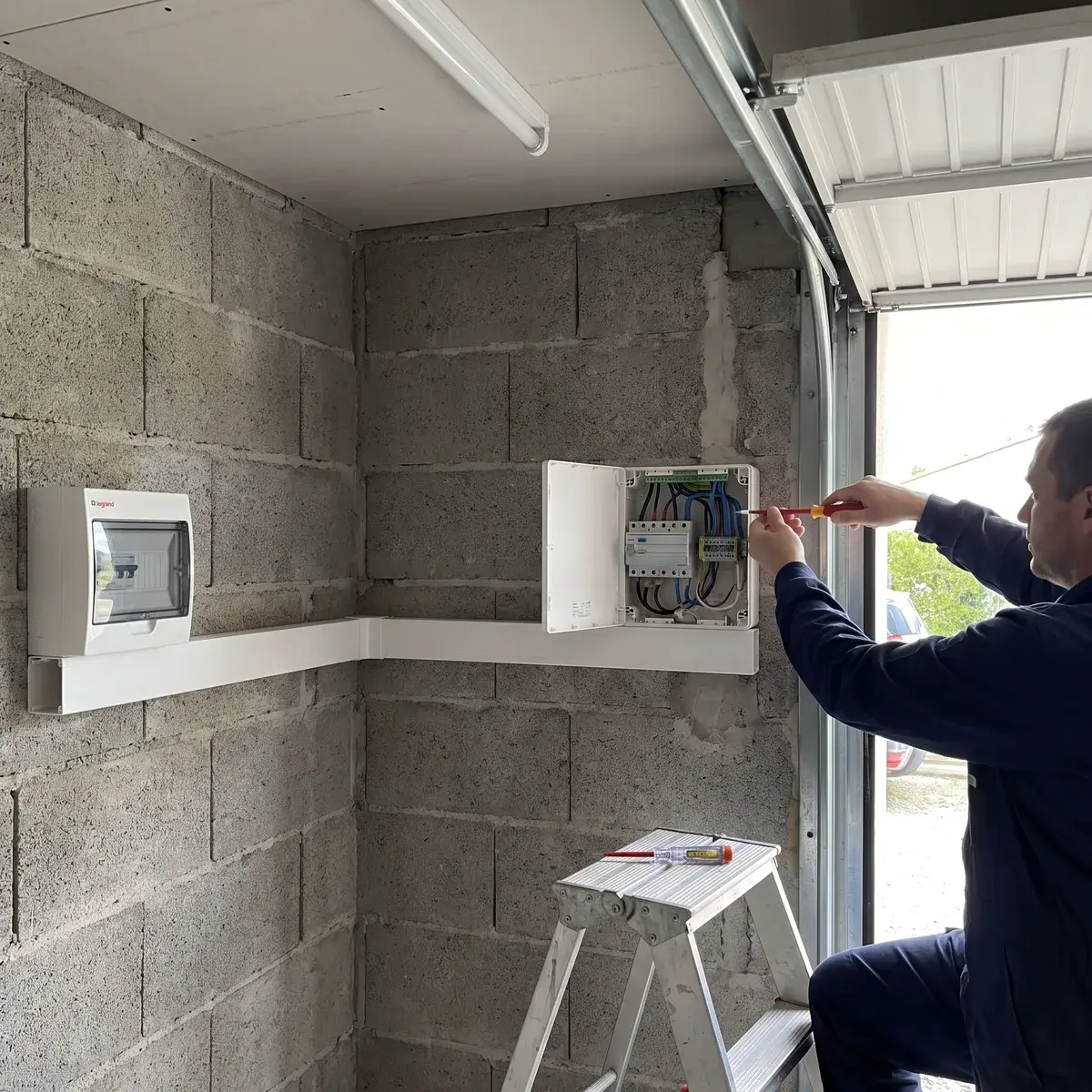 Un électricien raccorde une borne Hager witty start au mur d'un garage, la goulotte venant du tableau Legrand.
