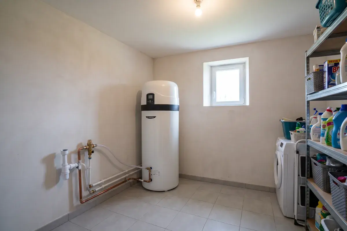 Chauffe-eau thermodynamique Ariston Nuos Plus S2 sur air ambiant, posé dans l’angle d’un cellier carrelé non chauffé, avec de l’espace libre autour de l’appareil.