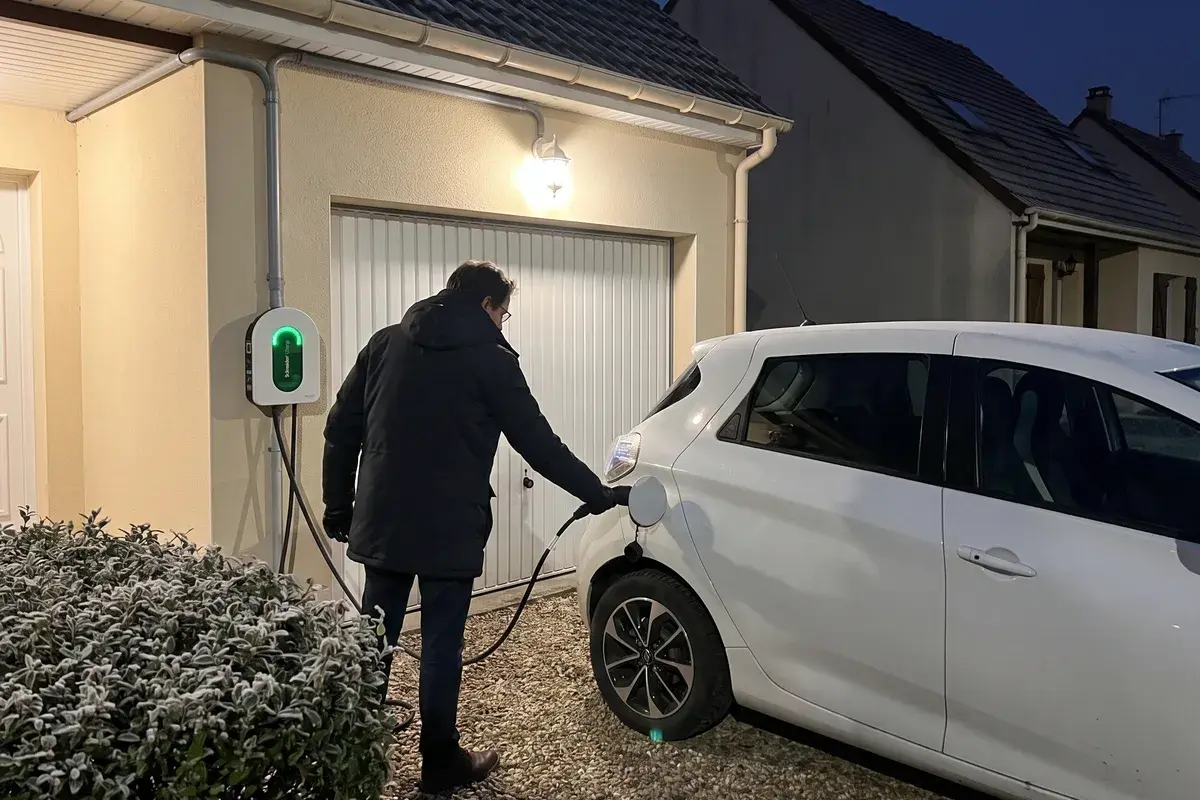 Un soir d’hiver, un particulier branche sa voiture électrique sur une borne Schneider Charge fixée à la façade de son pavillon.