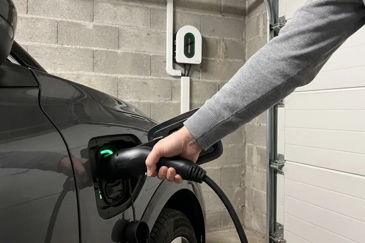 Main qui enfonce le connecteur Type 2 d’une borne Schneider Charge dans la trappe de recharge d’une voiture électrique, dans un garage en parpaing.