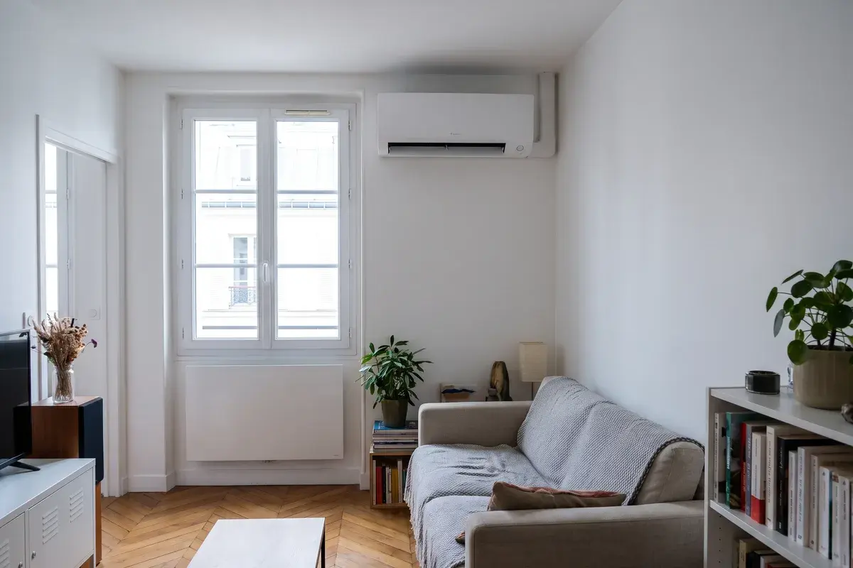 Unité intérieure murale Daikin Perfera installée au-dessus d’une fenêtre, dans le séjour d’un appartement à parquet.