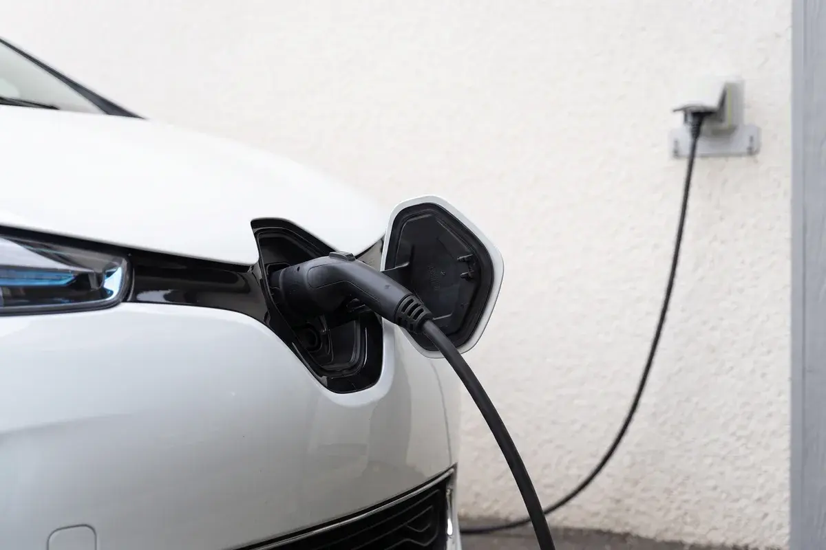 Gros plan sur le nez d'une Renault Zoe blanche, trappe relevée, avec un connecteur Type 2 branché dans la prise ; le câble rejoint une prise murale.