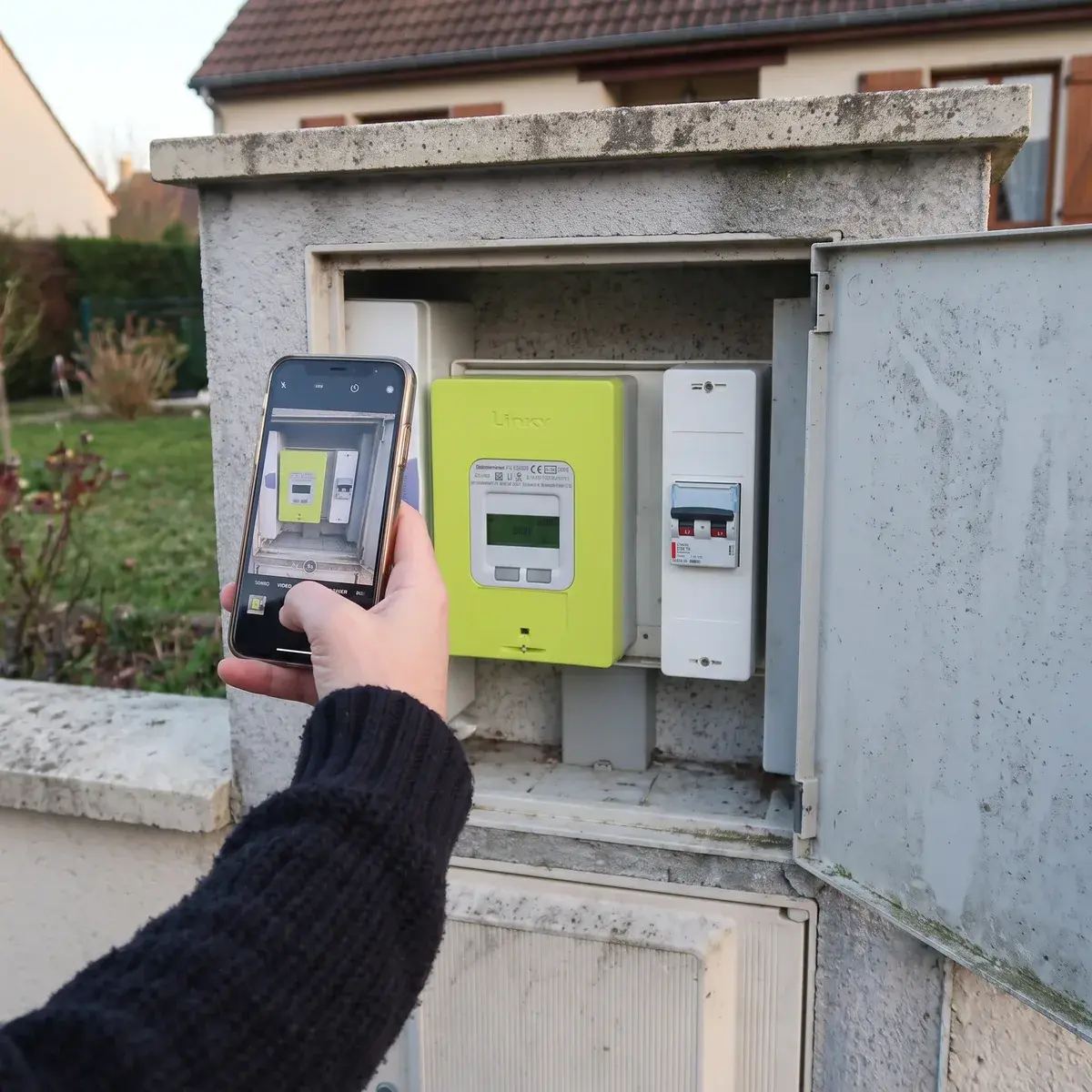 Compteur Linky dans un coffret encastré dans le muret d'un pavillon, photographié au téléphone pour relever l'index.