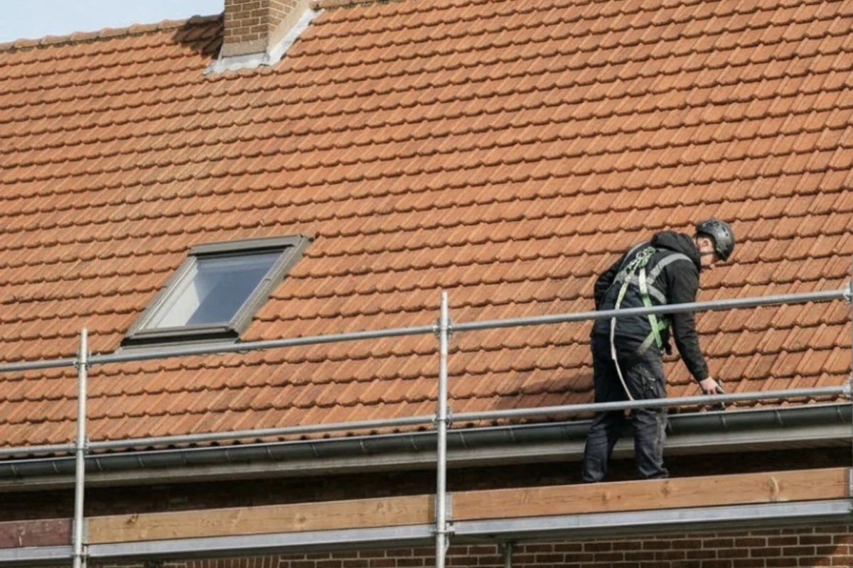 Installateur sur un échafaudage protégé devant la toiture avant la pose des rails