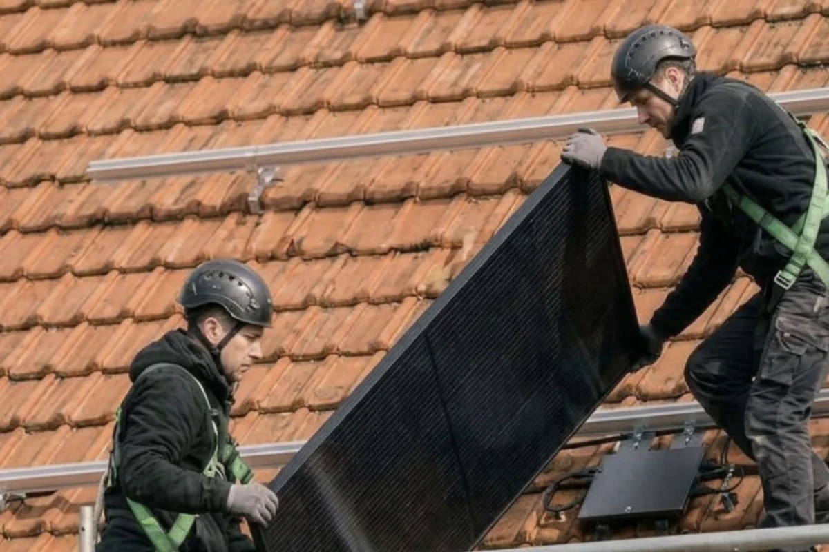 Deux installateurs en tenue de chantier déplacent ensemble un panneau photovoltaïque au-dessus des rails